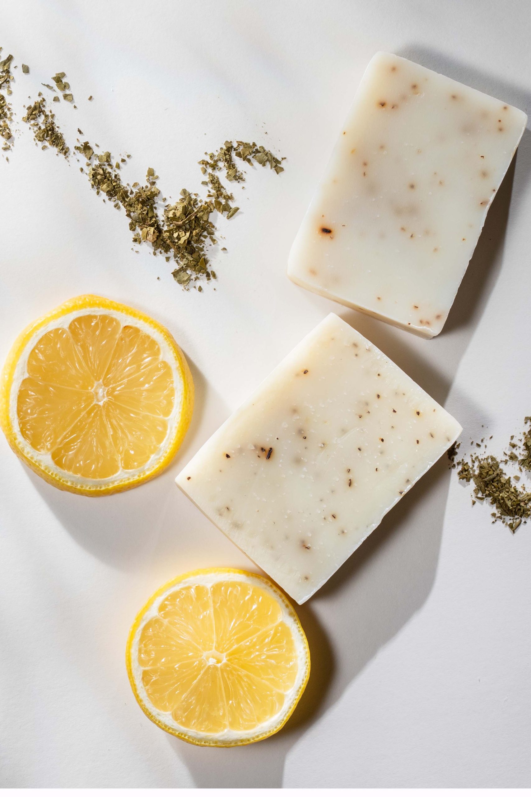 Flat lay of two handmade lemon tea bar soaps with a spoonful of tea leaves and lemon slices