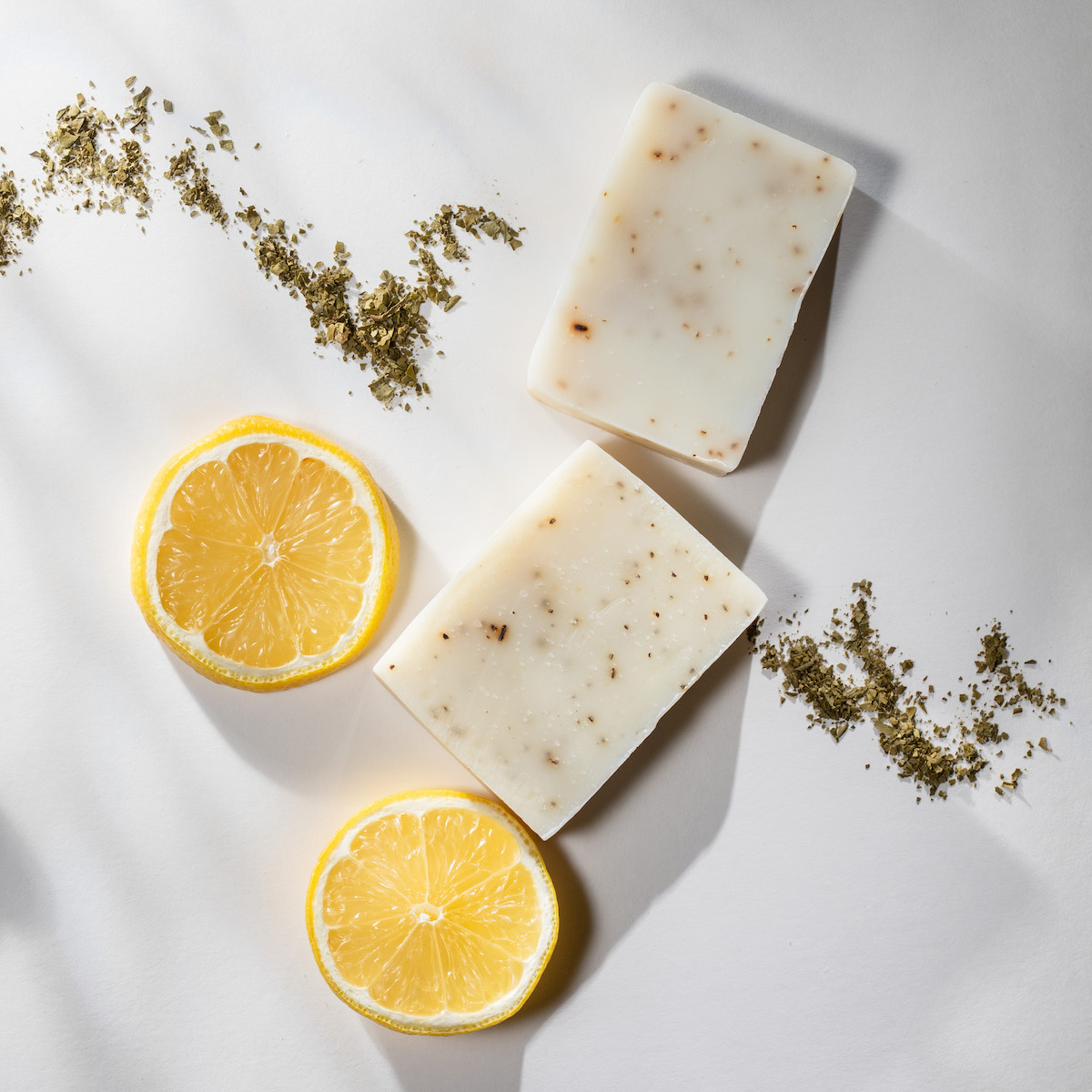 Flat lay of two handmade lemon tea bar soaps with a spoonful of tea leaves and lemon slices